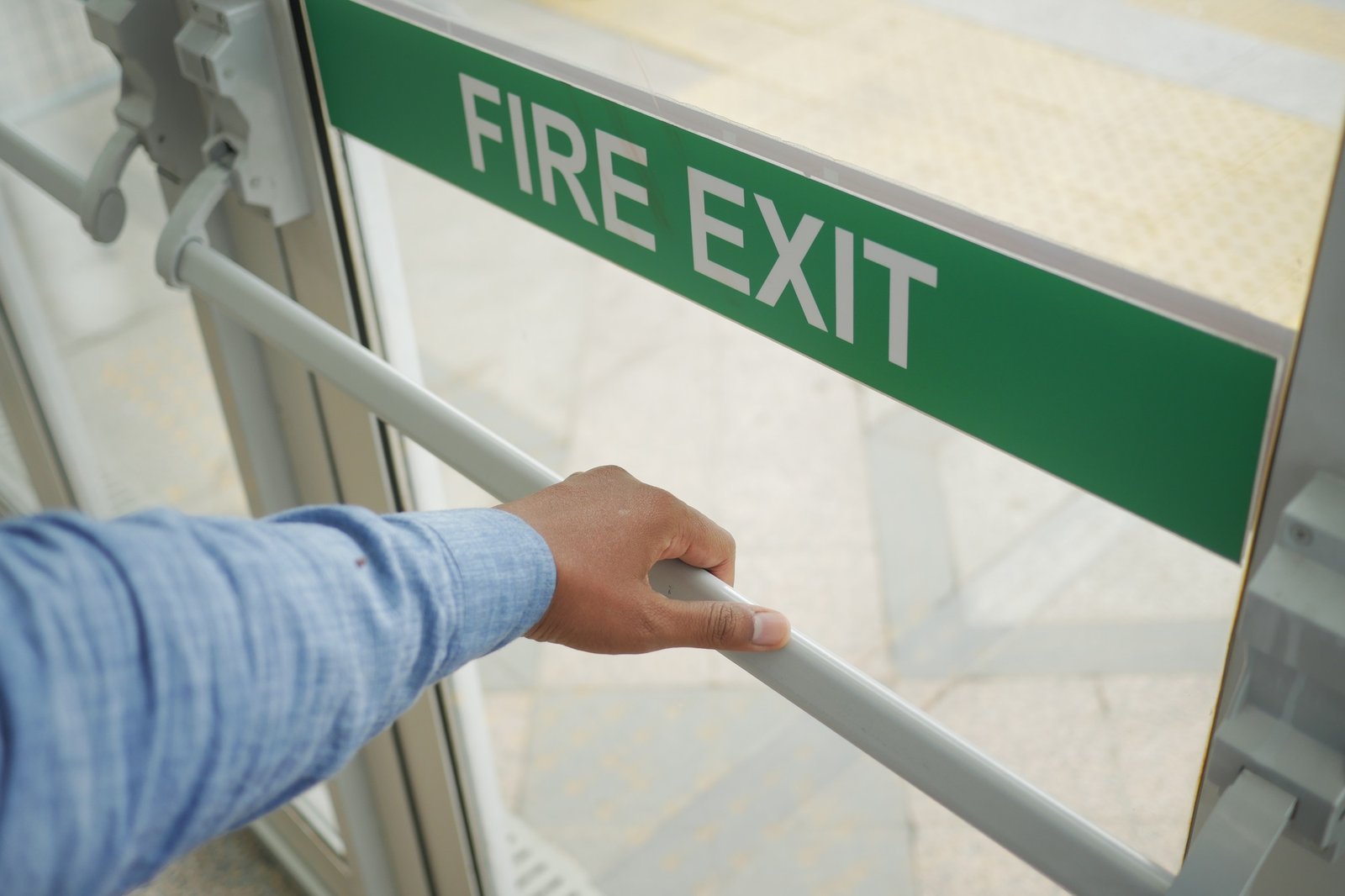 A person is using their hand to open a fire exit door for a vital emergency evacuation